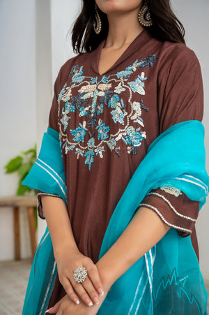 Model wearing Mocha Sea 3-piece khaadi silk outfit in mocha brown with aqua blue hand embroidery, paired with organza dupatta featuring colored pati borders