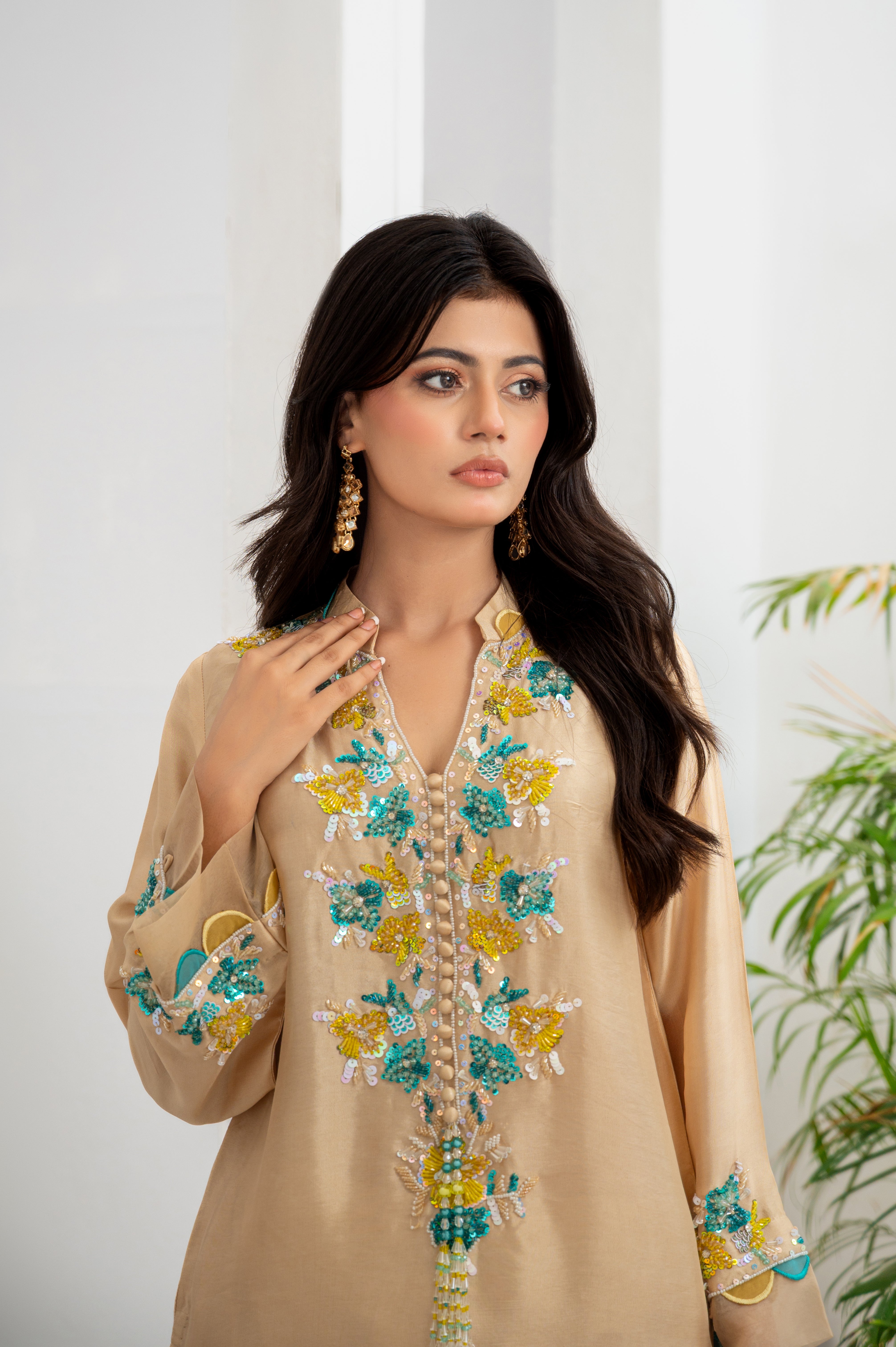 Woman wearing a beige embroidered shirt with floral patterns against a white curtain background